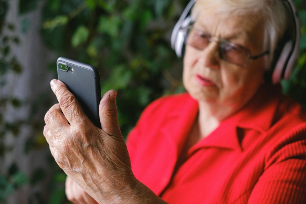 A senior lady looking at an accessible digital product on her phone with headphones.
